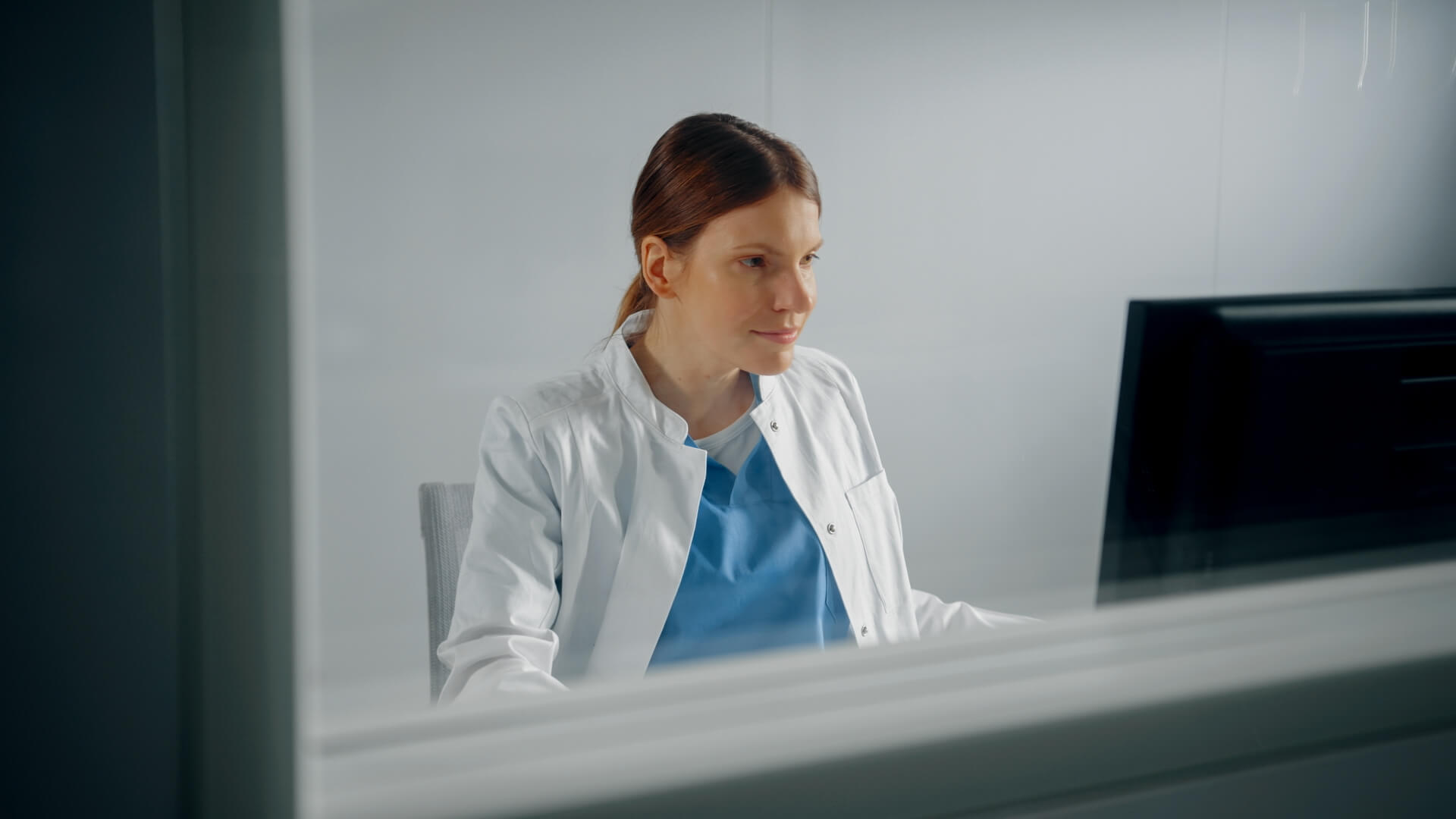 A physician seated at her desk, focusing on the computer screen
